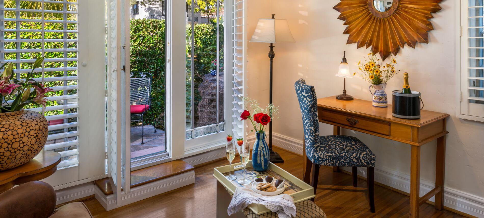 open door to private patio, blue chair under desk with container with sunflower, champagne in ice bucket, tray with refreshments