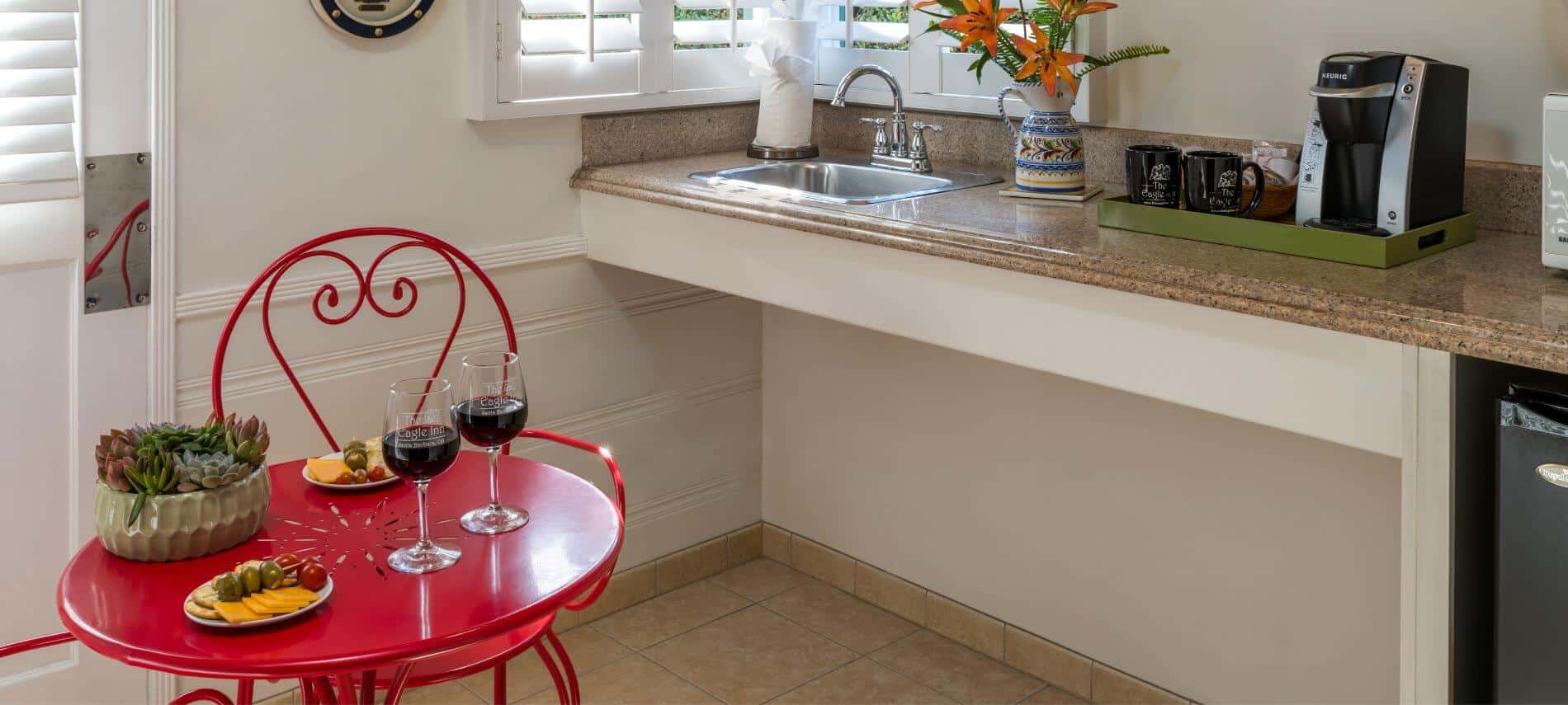 small tiled kitchenette with sink, coffee maker, microwave and refrigerator, round red metal table and chairs