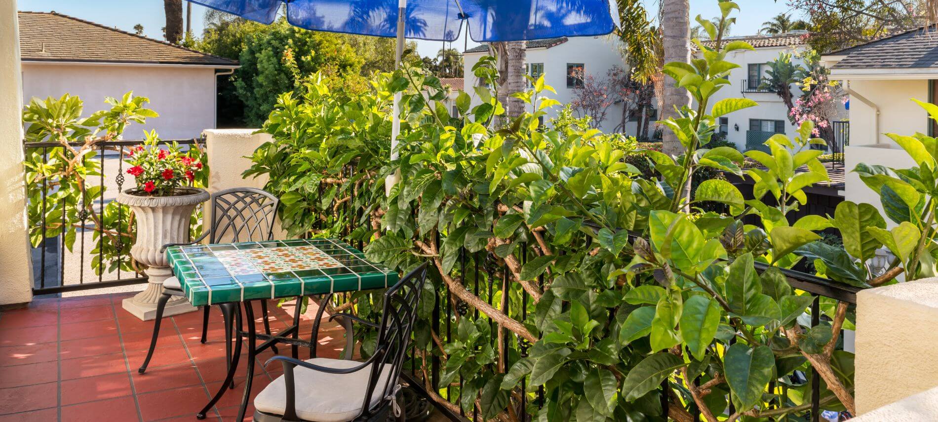 private patio surrounded by foliage with small square green and white table with tan cushioned metal chairs