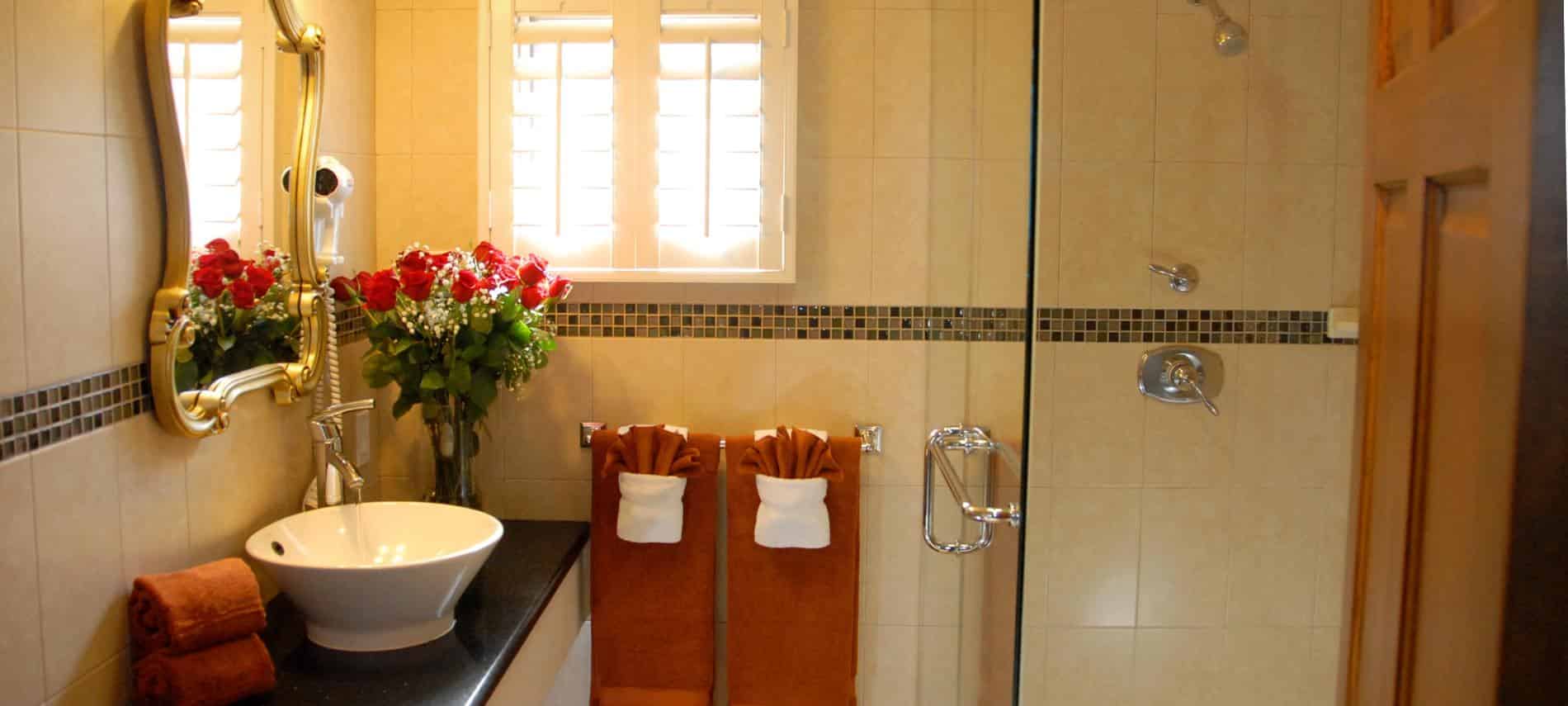 San Nicolas guest bath, small window, long black vanity top with white vessel bowl sink and tiled shower with glass door