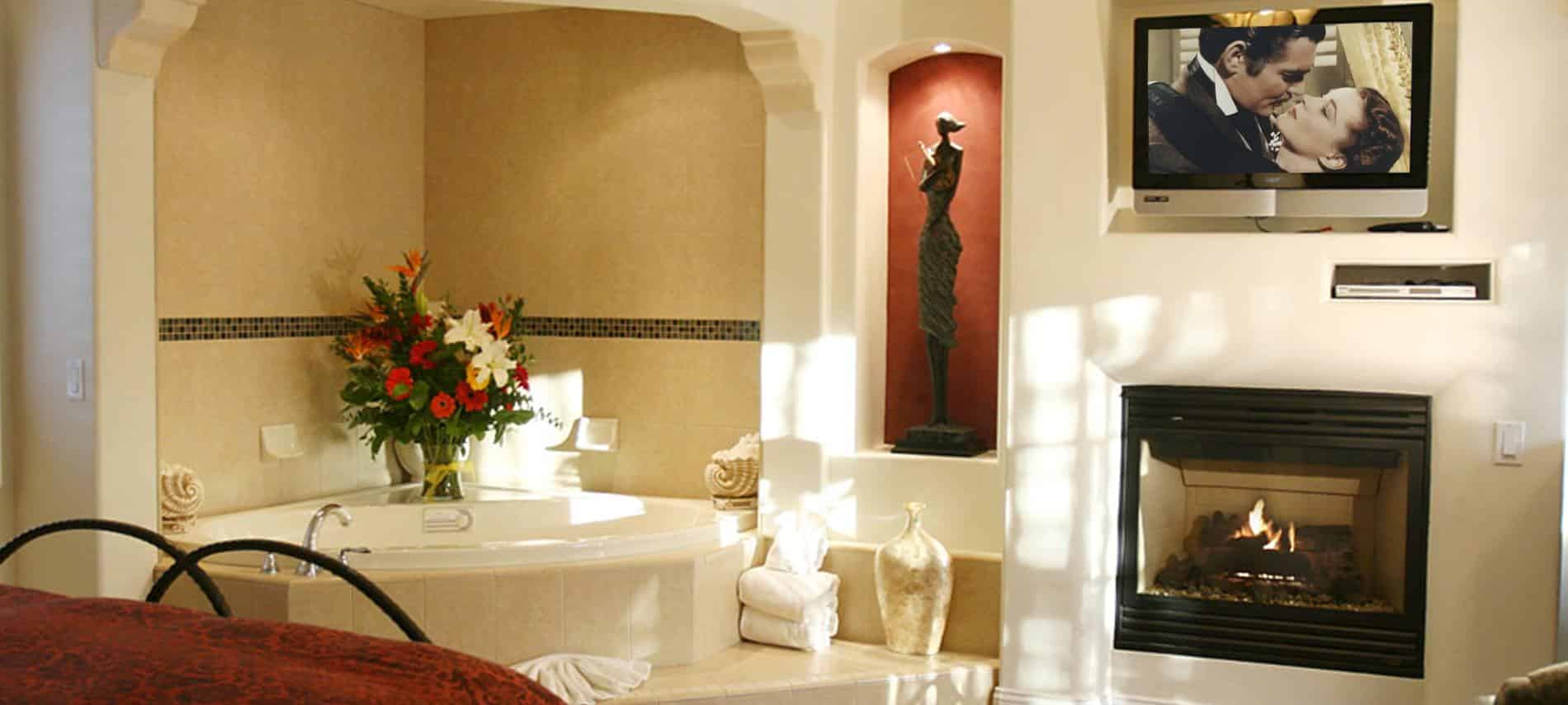 San Nicolas guest room with white walls, semi-enclosed corner tub, red niche with sculpture and light, fireplace and TV