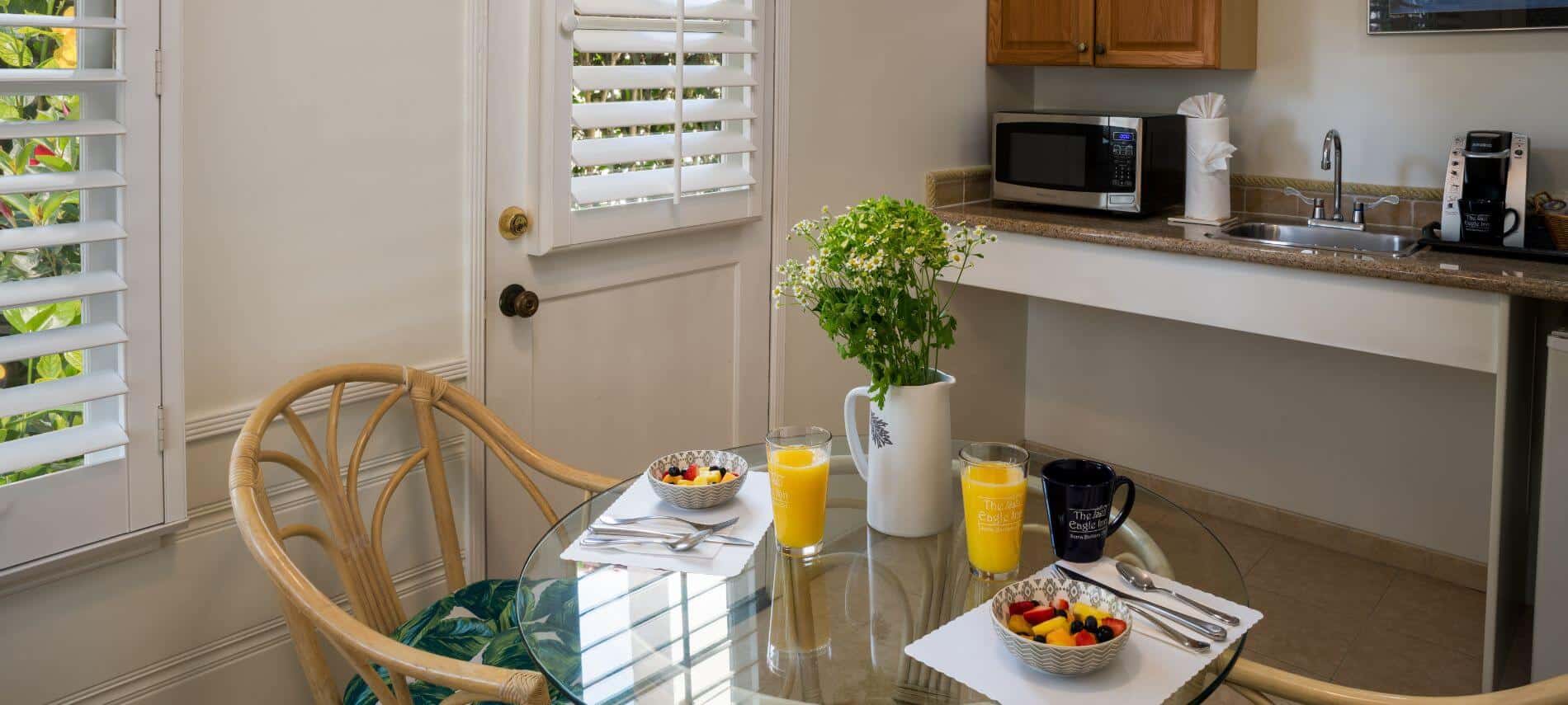 small kitchenette with round glass table with flower cushioned chairs, microwave, sink and coffee maker