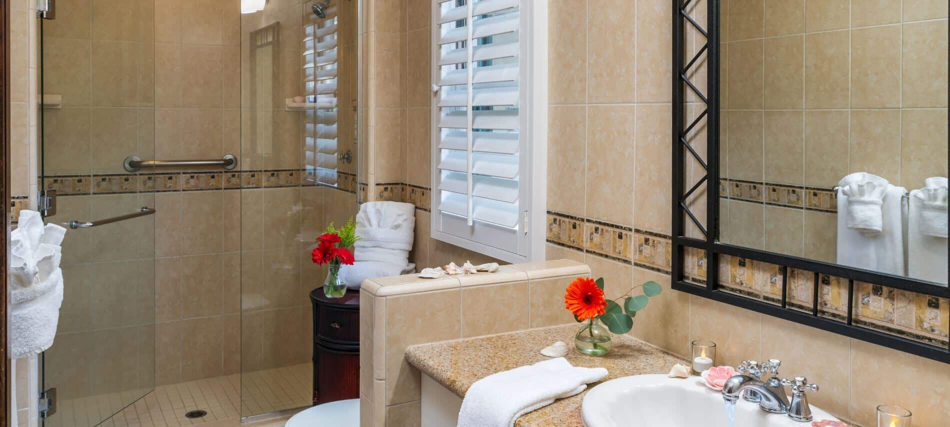tiled bathroom with glass enclosed walk-in shower with grab bar, white sink with black framed mirror hanging above