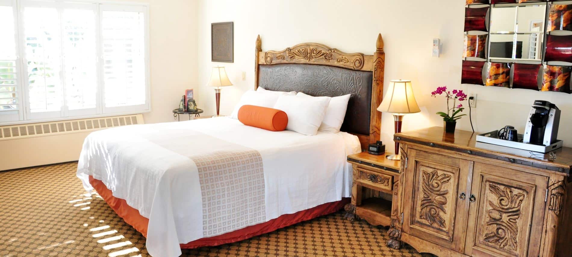 Superior King guest room with wood and leather headboard, wood nightstands, wood cabinet, coffee maker, and fresh flowers