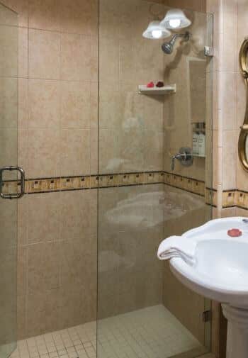 tiled bathroom with glass enclosed walk-in shower, white pedestal sink with white cloth on edge