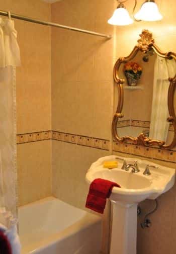 Deluxe King balcony bathroom with white pedestal sink, white tub surrounded by tile, and vintage mirror