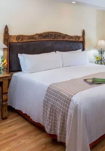 cream room with wood floors, king bed with wood and leather headboard, stands with lamps