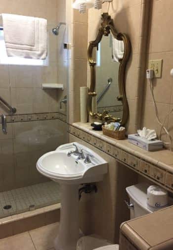 Queen bathroom with white pedestal sink and light brown tile shower