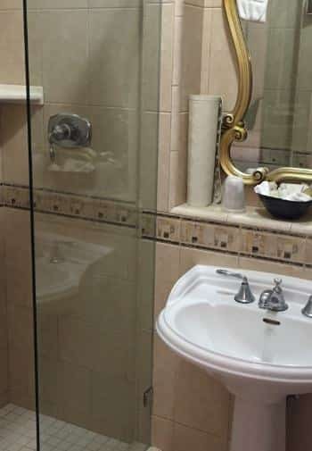 Queen bathroom with white pedestal sink and light brown tile shower with glass sliding door