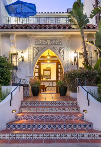 steps in between foliage leading into the building through a diamond shaped doorway, balcony on 2nd floor
