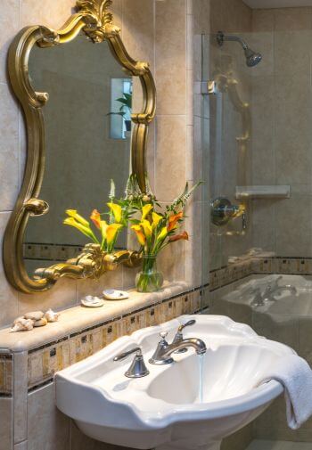tan tiled glass enclosed shower, white sink under gold trimmed mirror hanging on the wall