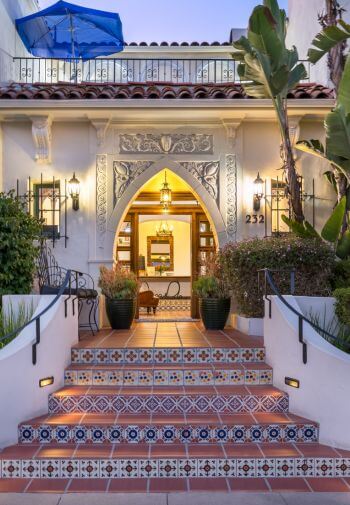 steps in between foliage leading into the building through a diamond shaped doorway, balcony on 2nd floor