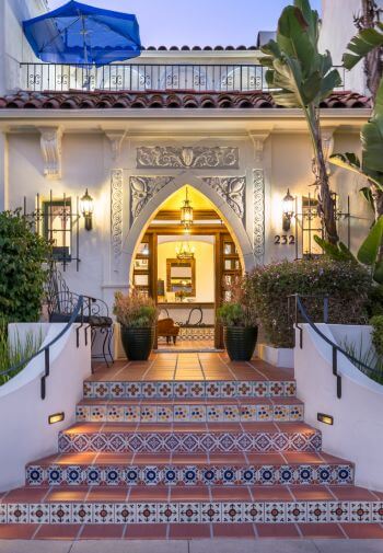 steps in between foliage leading into the building through a diamond shaped doorway, balcony on 2nd floor