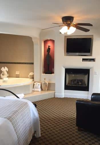 San Nicolas guest room with white walls, semi-enclosed corner tub, red niche with sculpture and light, fireplace and TV