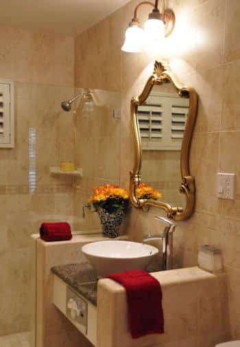 Santa Barbara guest bath with tiled walls and shower, glass shower door, white vessel bowl sink and gold mirror