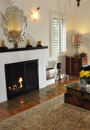 Santa Barbara guest room with shuttered window, fireplace with tile surround and black mantel, silver mirror, and wood floor