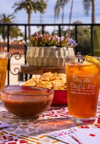 two glasses with the eagle inn logo filled with iced tea, chips and salsa in bowls sitting on table at dusk