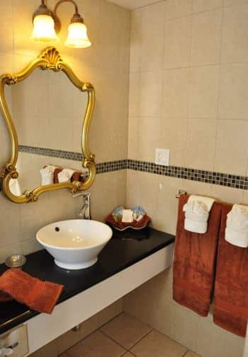 Santa Catalina guest bath with black vanity top, white vessel bowl sink, gold mirror, sconce light and tile floor