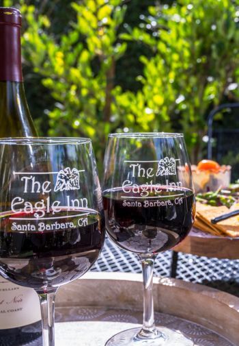 two wine glasses with the eagle inn logo filled with read wine on tray, wine bottle behind, charcuterie board behind