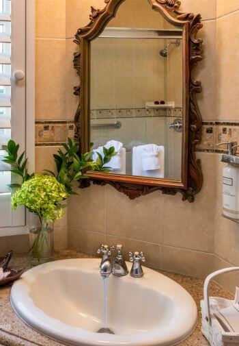 sink with running water under wood framed mirror with reflection of tiled shower with hanging towels