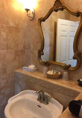 Double queen bathroom with white pedestal sink, tiled walls, and vintage mirror