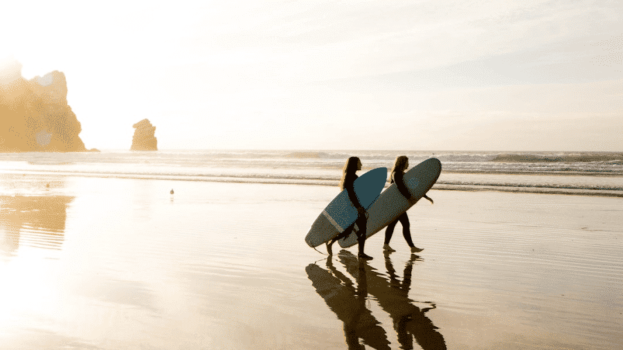 Two Surfers holding boards standing in water walking toward waves